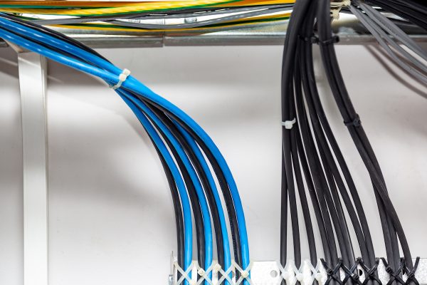 The black and blue cable wires are symmetrically secured with white cable ties to the metal cable tray, ladder on a white background. Cable management. Horizontal orientation. High quality photo.